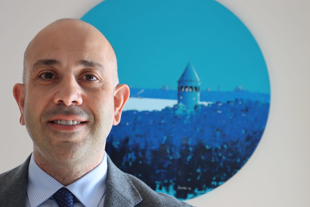 Avukat İltan Ekmekçioğlu mavi İstanbul görselinin önünde portre